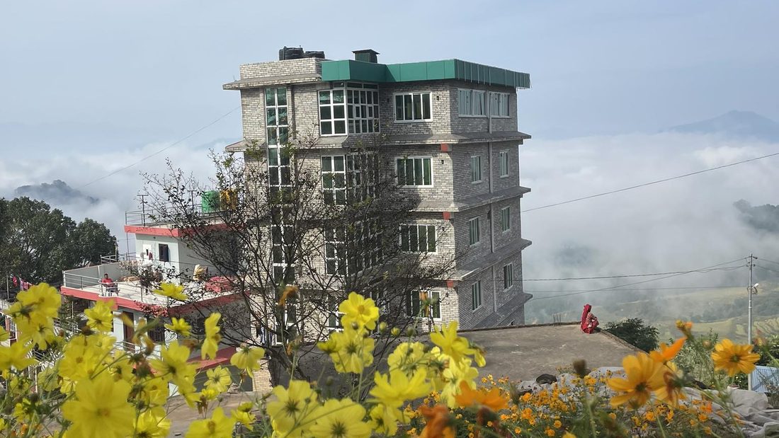 Hotel Yatri standing on the ridge at Sami Dadha above a sea of cloud, with cosmos flowers in the foreground